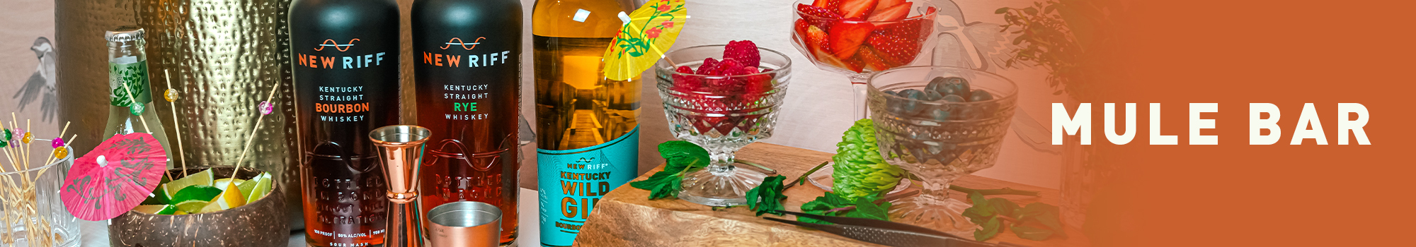 Mule Bar. Bottles of New Riff Bourbon, New Riff Rye, and New Riff Gin next to cups with fruit, herbs and cocktail umbrellas.